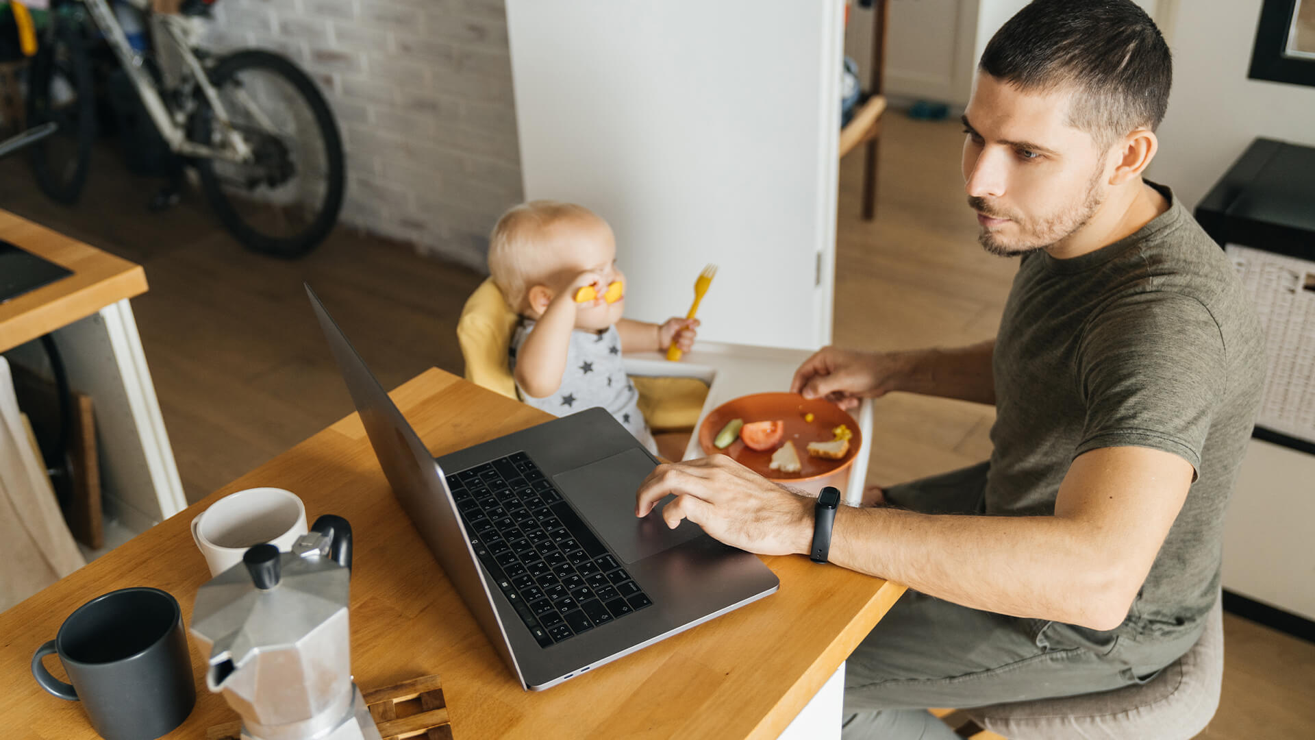 Dad working from home at a laptop while feeding his baby