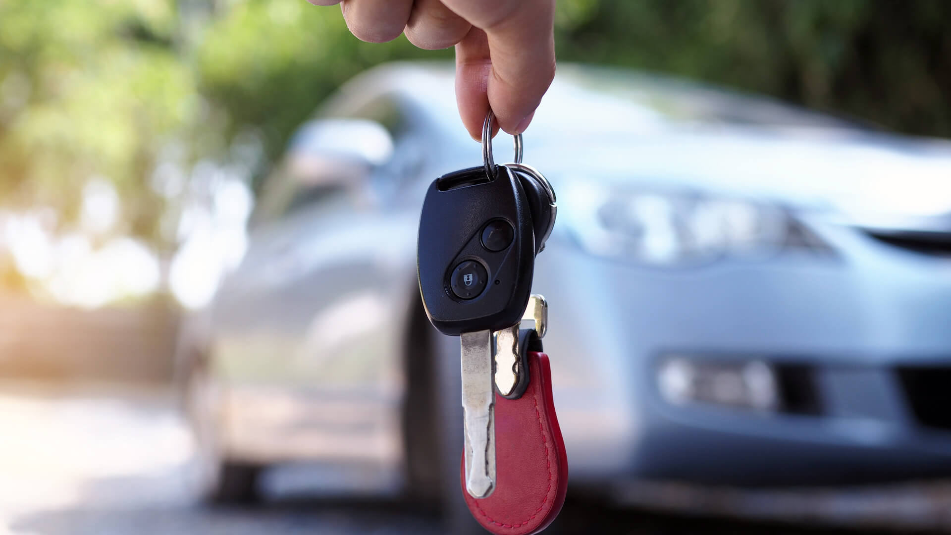 Closeup of ghand holding car keys. A car is in the background, out of focus.