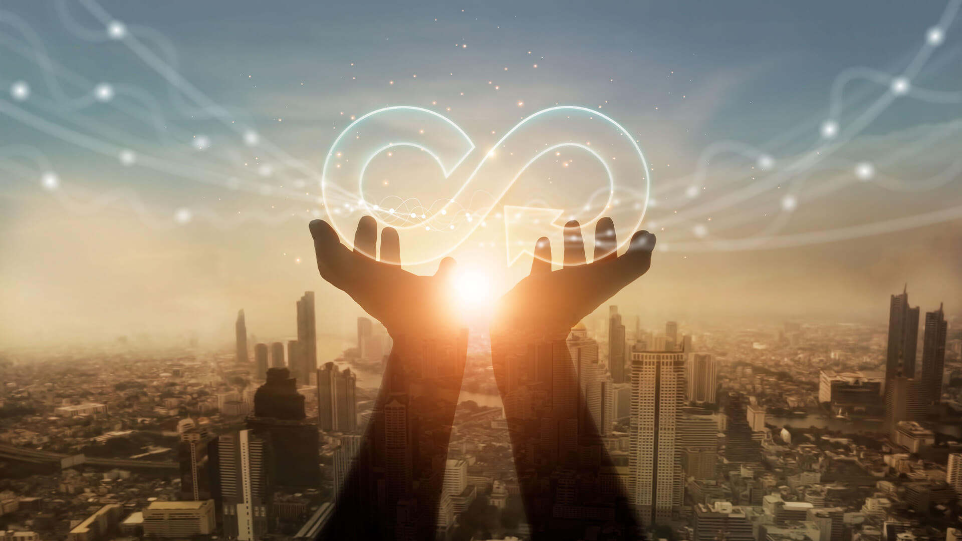 Hands holding an infinity symbol over a city skyline at sunset