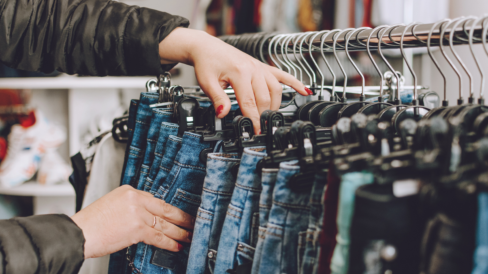 Woman chooses jeans in a store. Lots of clothes in the store.