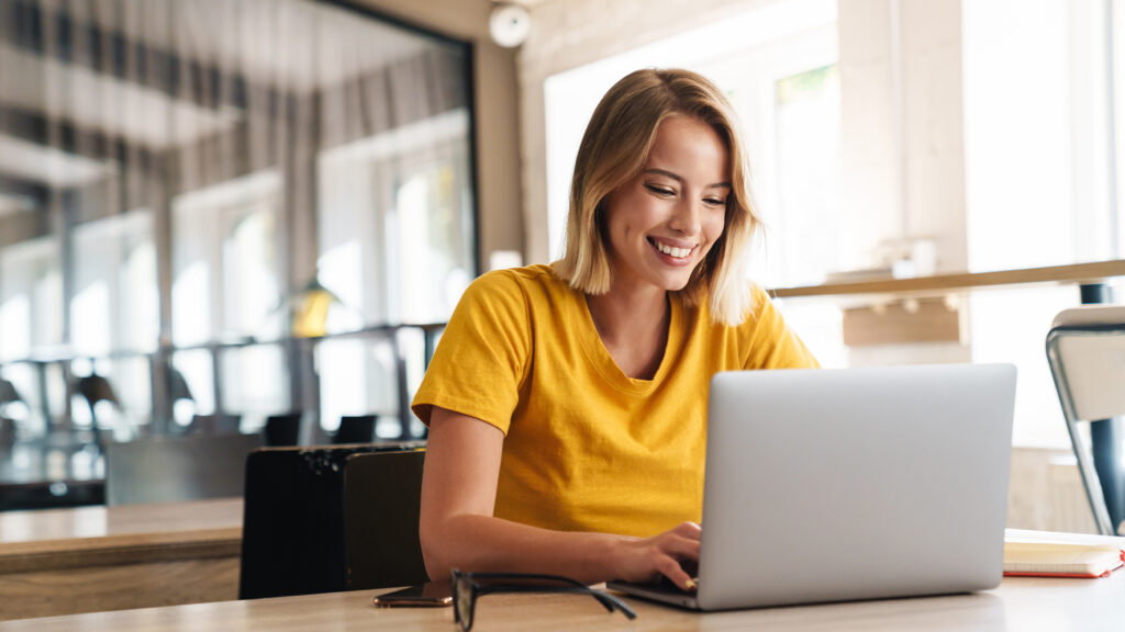 Photo of joyful nice woman using laptop and smiling while sitting