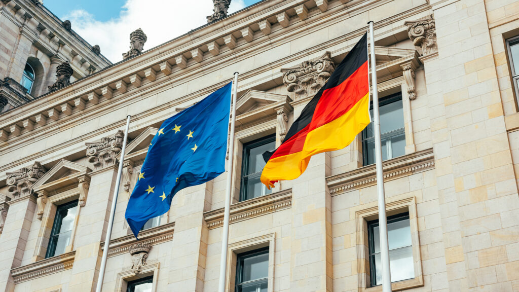 looking up at the flags of the european union and Germany waving in the wind in front of the Reichstag in Berlin.