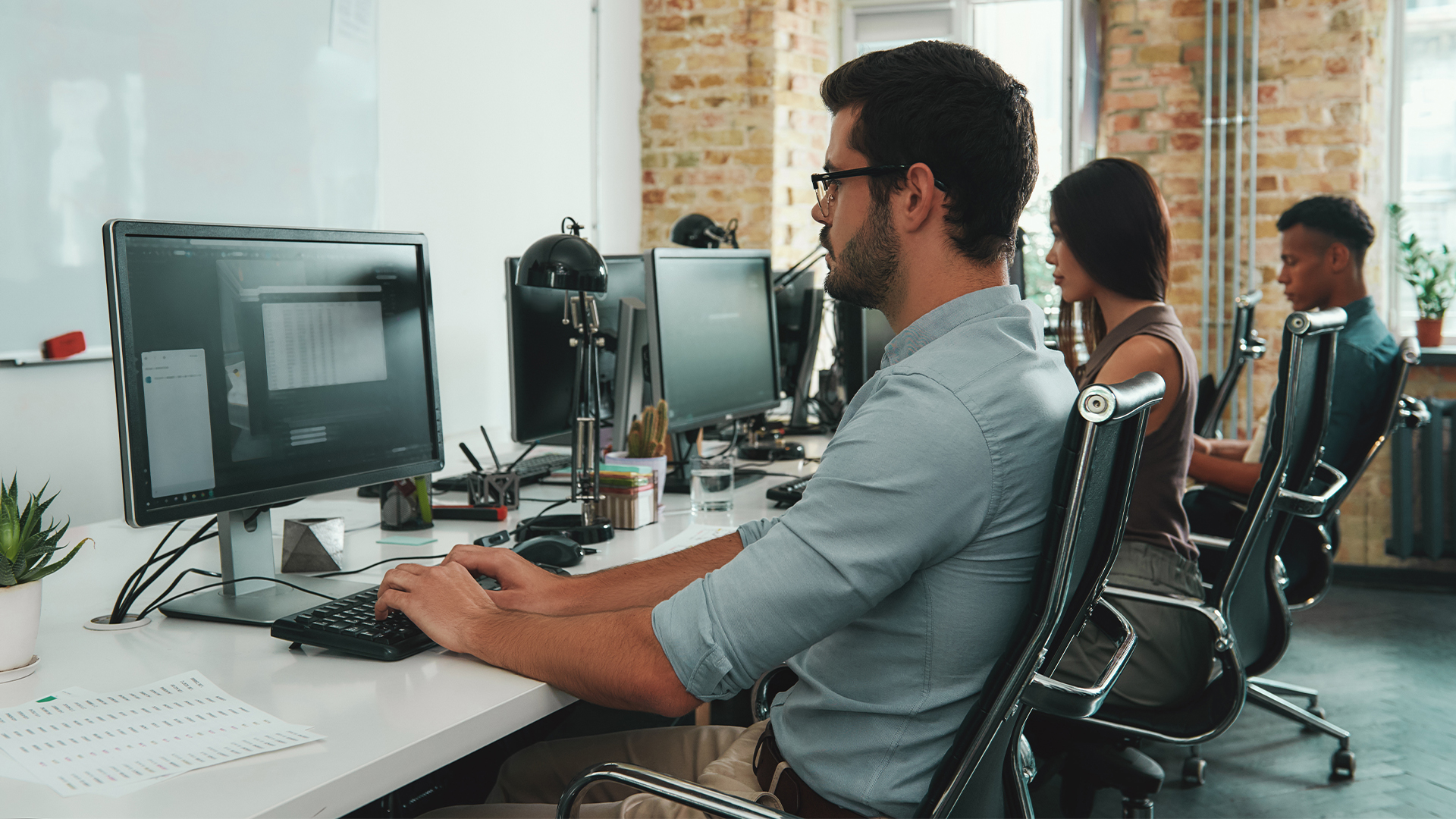 Focused at work. Side view of young busy employees working on computers while sitting at desk in modern open space